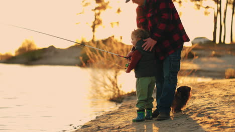 idyllic family scene on coast of river or lake in sunset time little boy and father are fishing