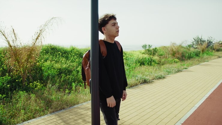 Man With A Backpack On The Sidewalk Waiting For The Bus To Come