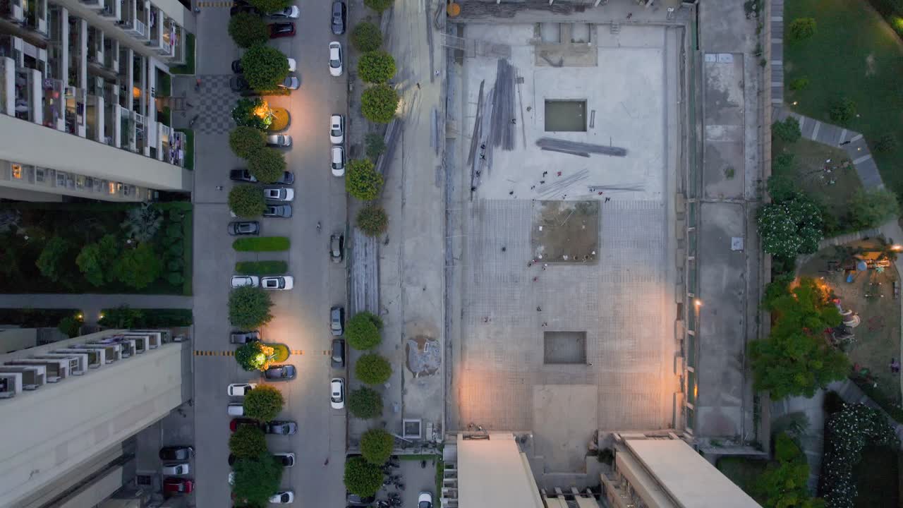 Aerial drone shot at night flying between skyscrapers parking over undr construction building and pool tennis showing the under construction and upgradation housing complexes in Gurgaon