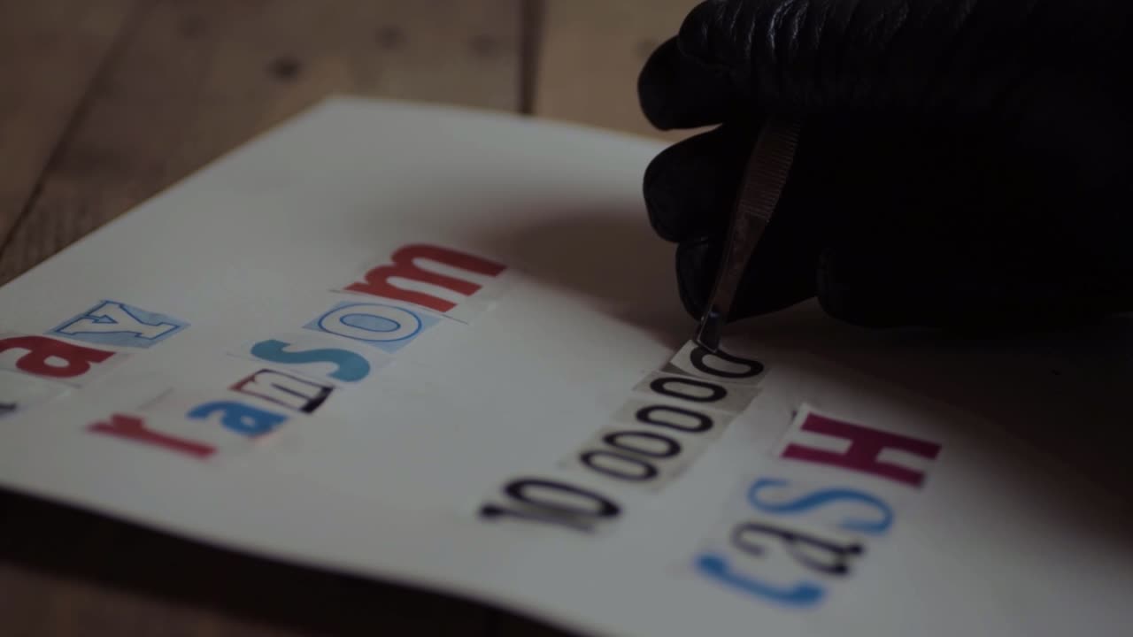 Kidnapper in black gloves making a ransom note for cash