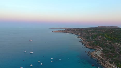 Vistas-De-Drones-De-La-Mundialmente-Famosa-Playa-De-Konnos-En-La-Isla-Mediterránea-De-Chipre-A-última-Hora-De-La-Tarde-Después-Del-Atardecer-Con-Agua-De-Mar-Turquesa-Clara