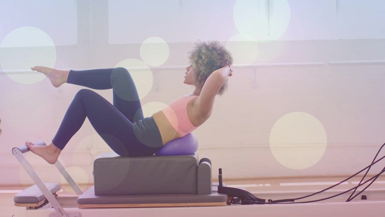 Donna che fa Pilates, esegue sollevamenti per il core, con i piedi appoggiati alla footbar e una palla viola dietro la schiena, con effetto bokeh che accentua il core.