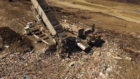 Massive-cargo-truck-unloading-garbage-into-landfill,-aerial-drone-orbit-view