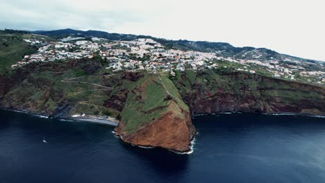 Establishing-aerial-dolly-view-across-Ponta-du-Garajau-green-island-coastline,-Madeira,-Portugal
