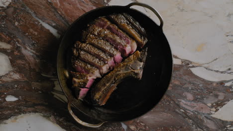 Top-down-shot-of-a-ribeye-steak-being-plated-into-a-cast-iron-pan