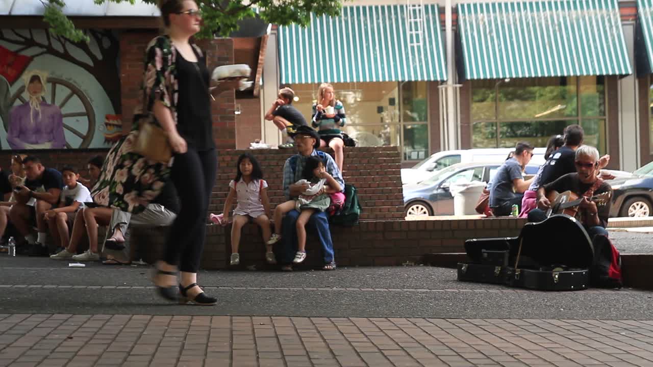 Tourists relax and eat by guitar player in OBryant Square in Downtown Portland