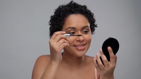 beleza, maquiagem e cosméticos conceito sorrindo bela jovem mulher afro-americana aplicando rímel sobre fundo cinza