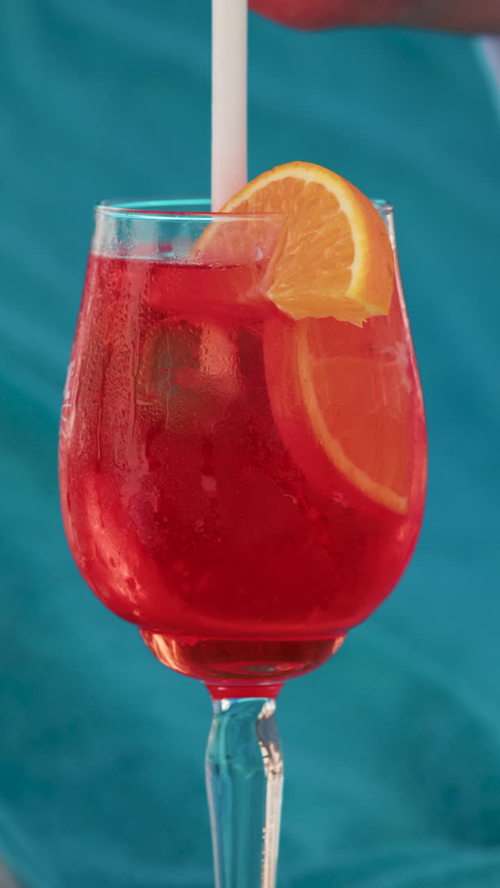 Close up of a refreshing red orange cocktail with orange slice and ice cubes, captured outdoors on a sunny day in Cannes. Vertical