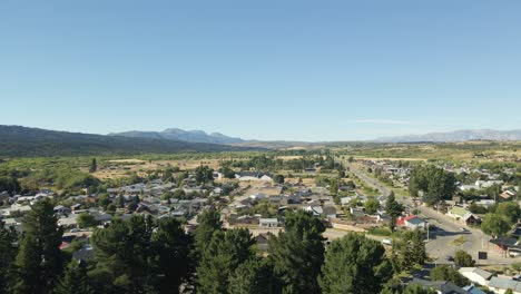 Aerial-pan-left-of-Trevelin-town-houses-surrounded-by-forest-and-Andean-mountains,-Patagonia-Argentina