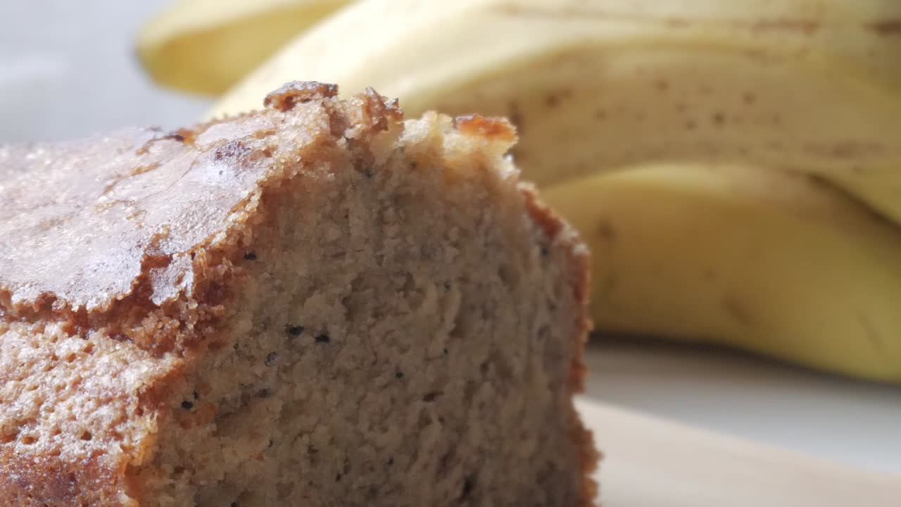 sartén derecha de pan de plátano cortado por la mitad en una tabla de madera con un plátano en la parte de atrás.