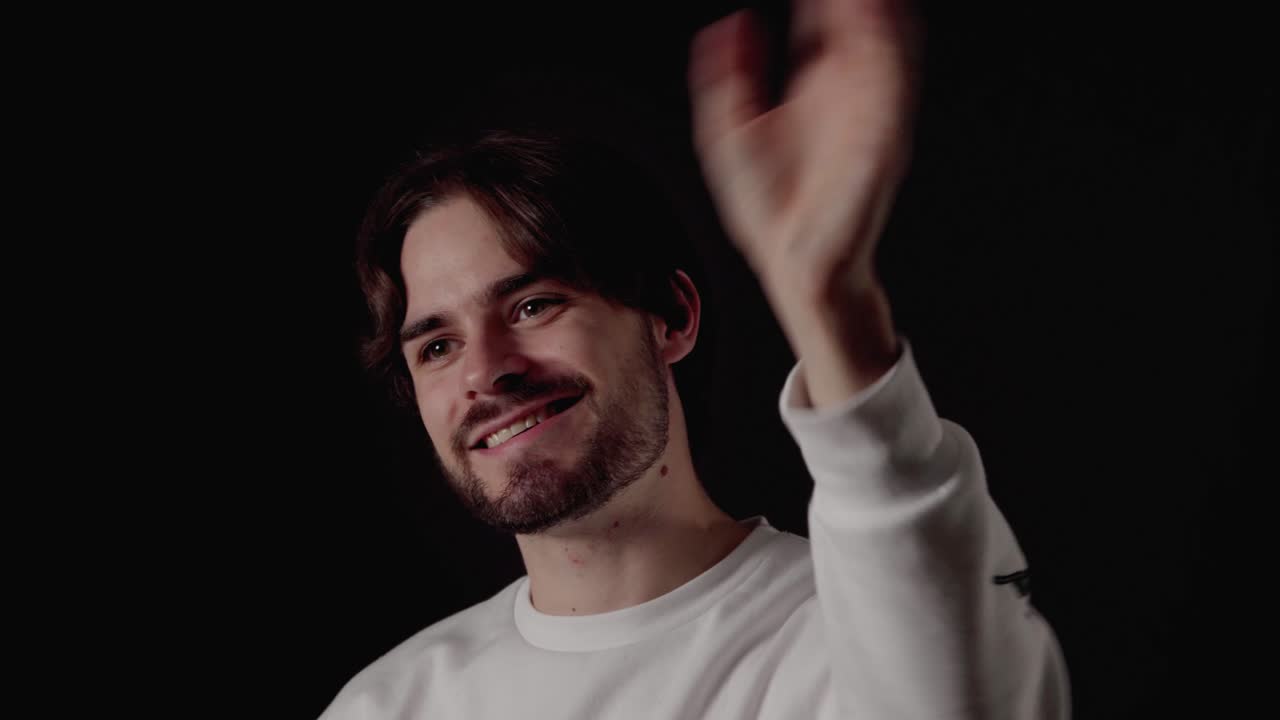 joven de moda saludando a la cámara, gesto de bienvenida, cerca, fondo negro