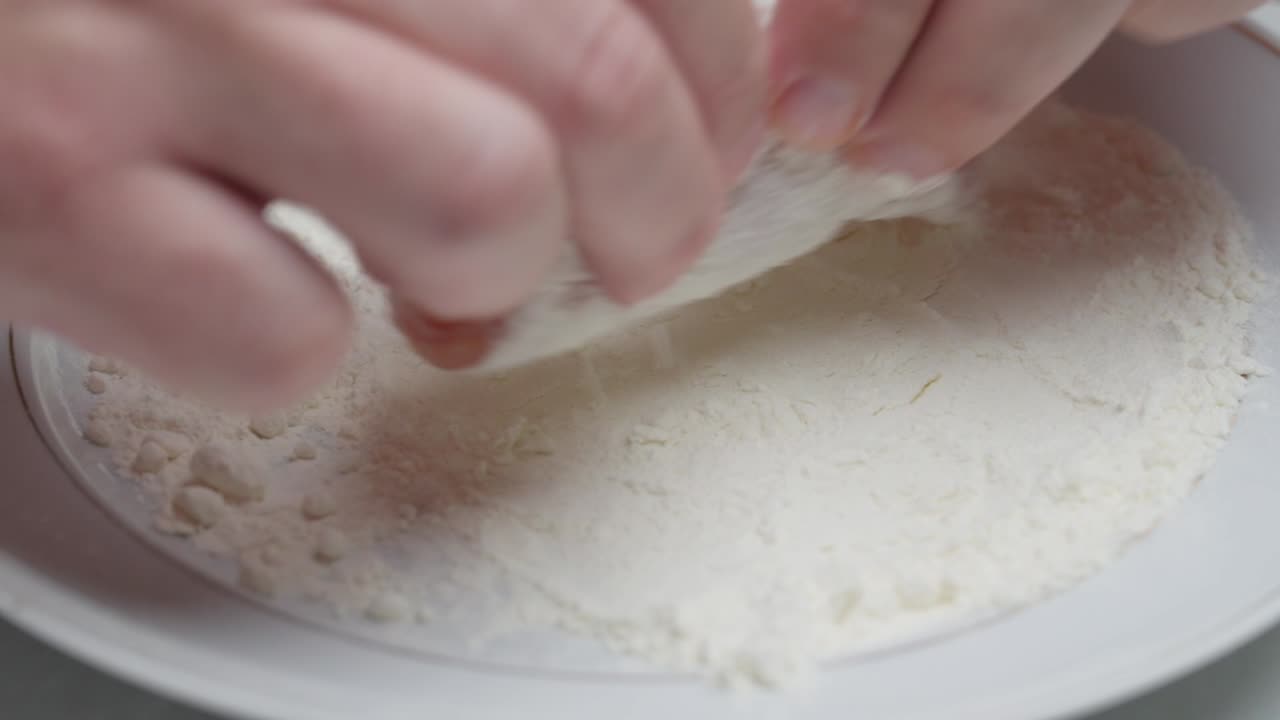 Close-up of rolled chicken meat being coated with flour during cooking prep