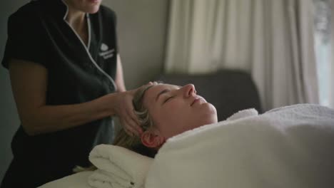 massage practitioner holding head of young, blonde client on table