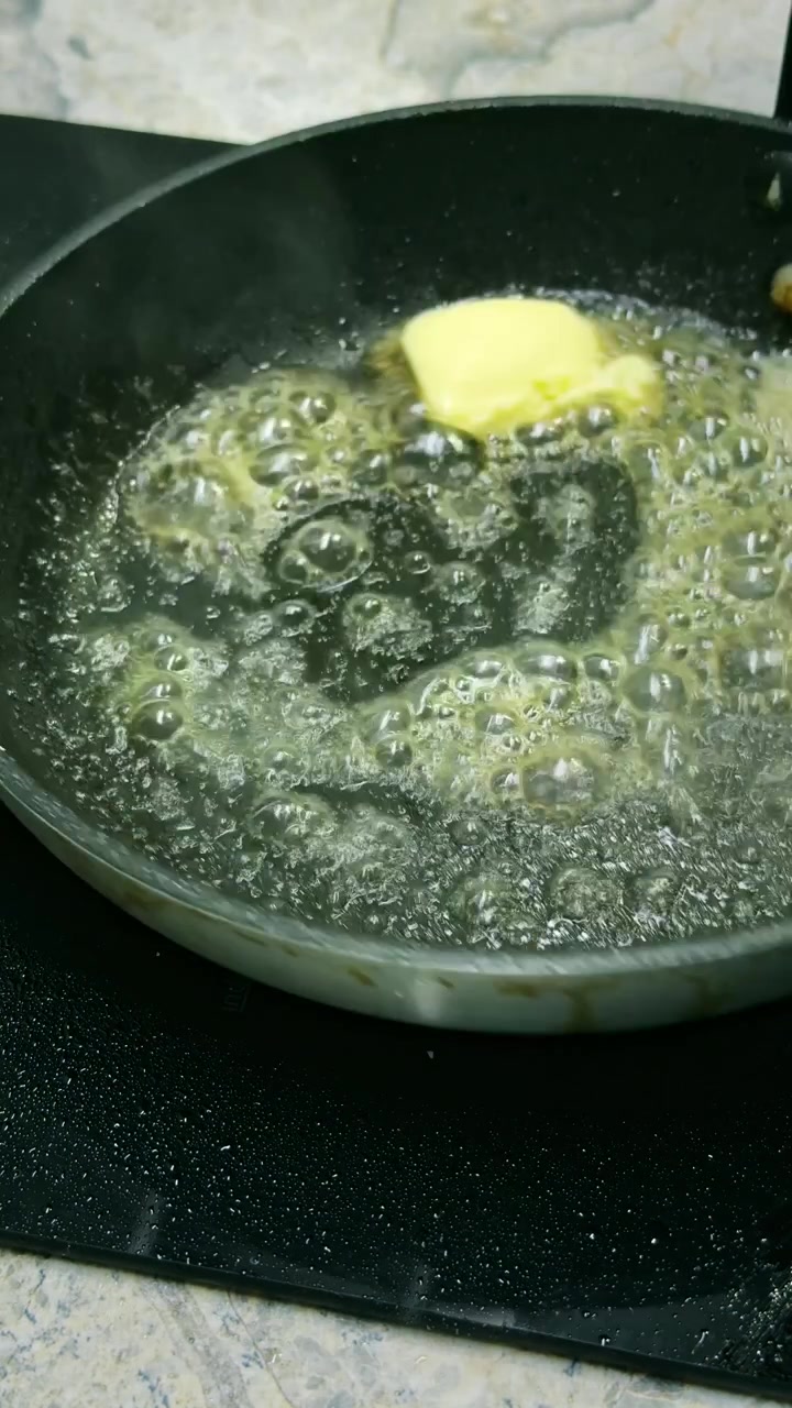 Close-up of a chef swirling melted butter around a hot frying pan before cooking. Vertical 4K food preparation footage showing an essential cooking technique.