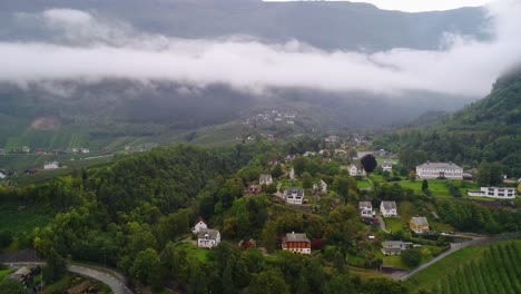 Panorámica-Aérea-Del-Pueblo-De-Ullensvang-Y-Viñedos-Con-Montañas-Distantes-En-Noruega