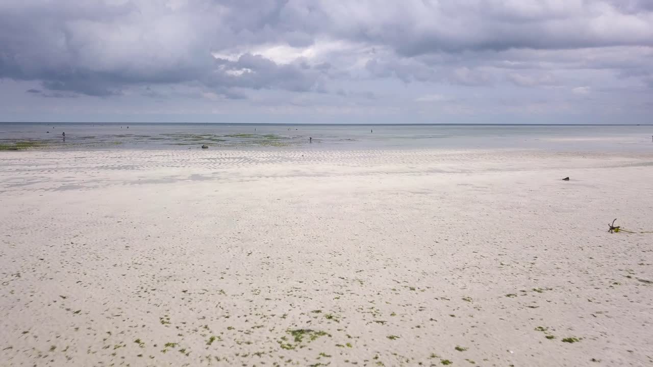 Aerial low flying over beach during low tide, people and stranded wooden boat