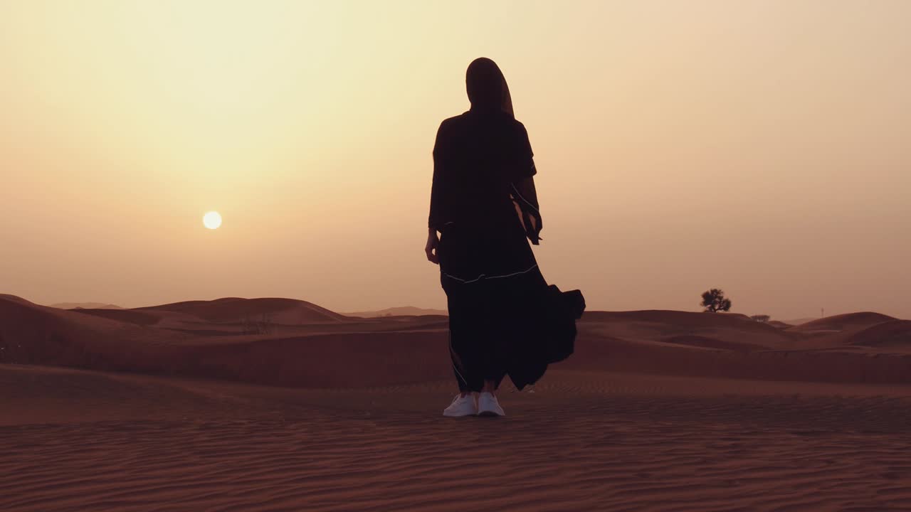 mujer musulmana de pie cerca de la mezquita en el desierto. viento fuerte oriente medio paz sin guerra