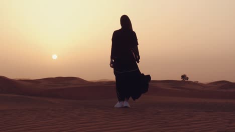 mujer musulmana de pie cerca de la mezquita en el desierto. viento fuerte oriente medio paz sin guerra