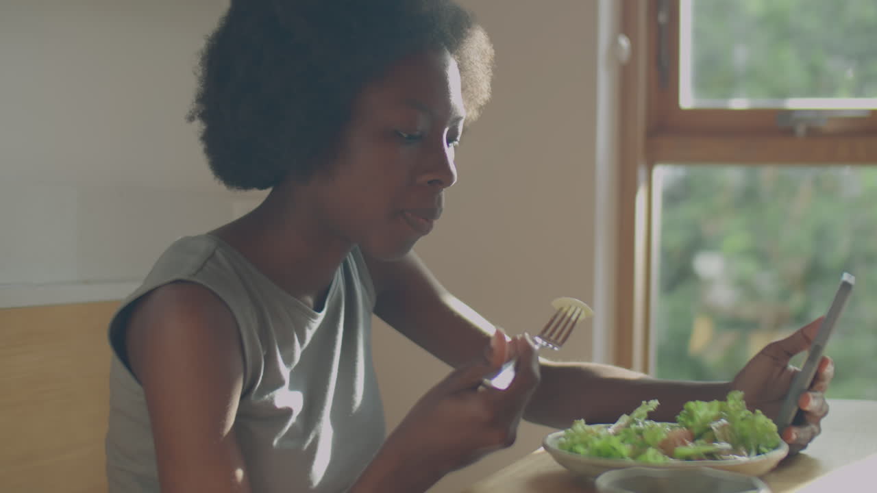 Black Woman Using Phone while Eating at Home