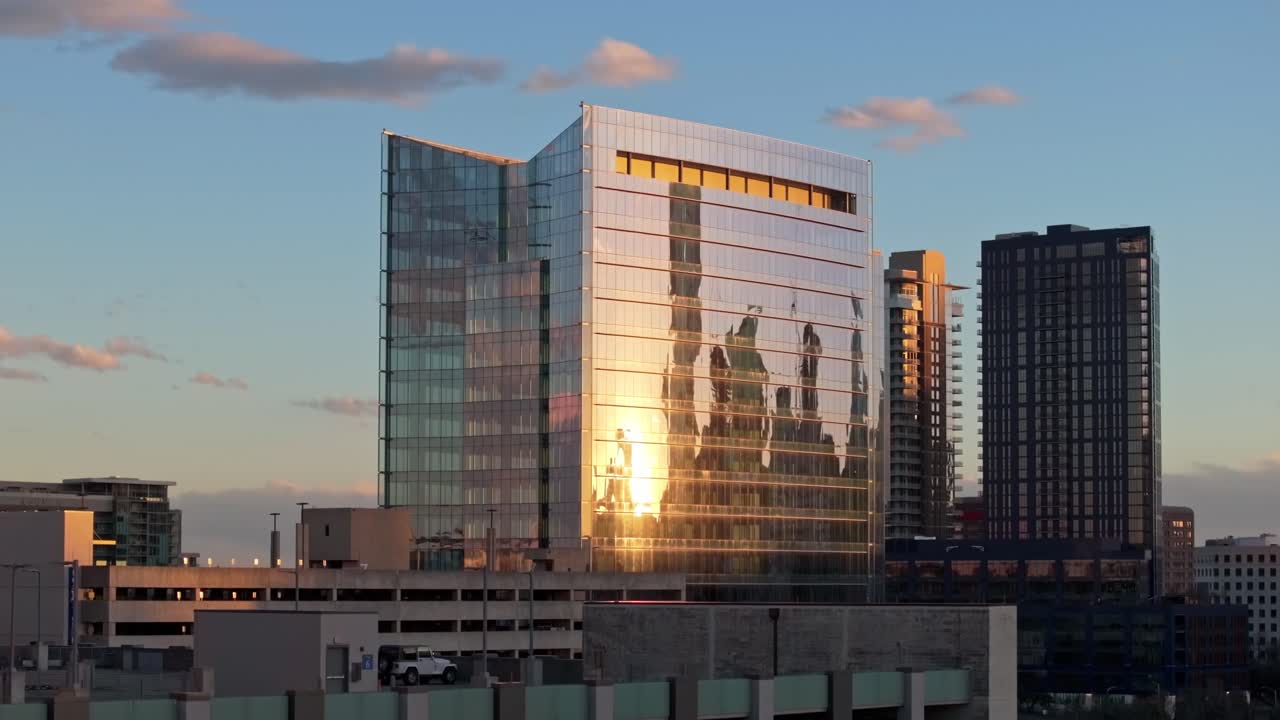 A zoomed in drone shot with parallax increasing elevation and centered on a parking garage and a building near the University Medical Center in Austin Texas with sunset reflecting off the windows