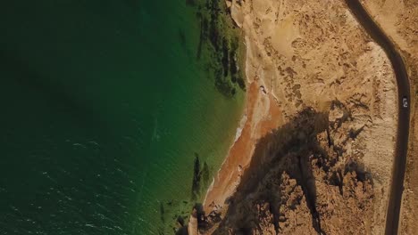 Landing-drone-shot-on-golden-sand-beach-asphalt-road-vehicle-driving-seaside-landscape-in-sunset-time-summer-tropical-climate-road-trip-adventure-green-water-wave-Iran-Qatar-natural-tourist-attraction