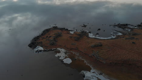 Aerial-view-descending-across-Stokksnes-coast,-peaceful-icy-Icelandic-seascape-reflecting-clouds