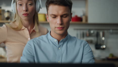 retrato de un hombre de negocios trabajando remotamente en casa mientras su esposa baila con auriculares