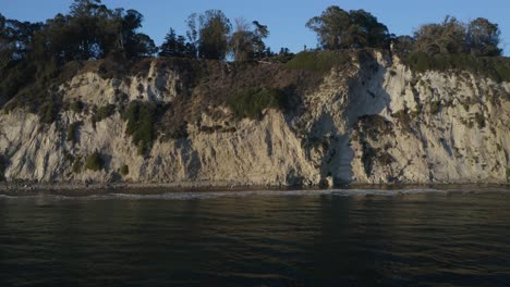 Drone-Flies-Backwards-Revealing-Dramatic-Coastal-Landscape-with-Mountains-in-Background