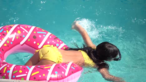 una niña linda en un traje de baño acostada en un círculo inflable de rosquilla. el niño nada sobre un fondo azul