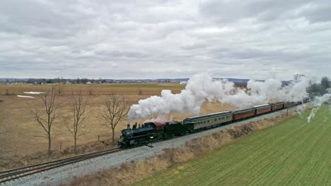 una vista aérea de un tren de vapor con un dron que sigue a un lado soplando humo y vapor viajando por el campo en un día de invierno