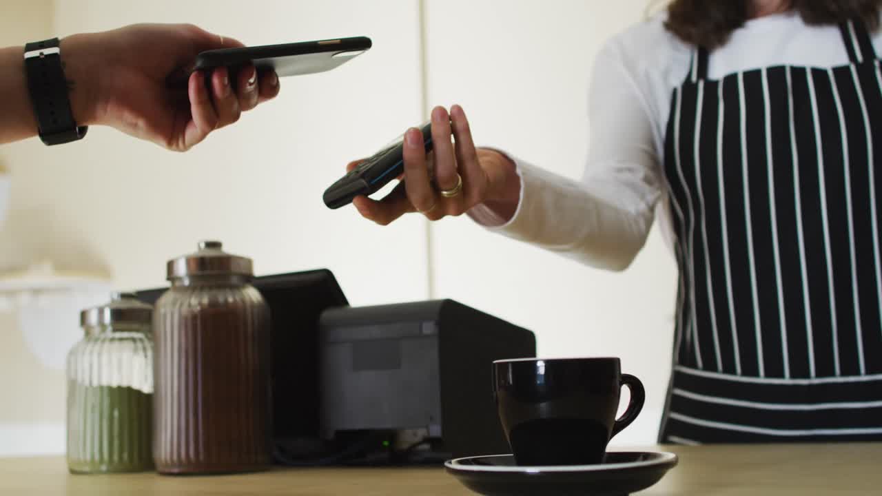 Cliente caucasica che usa lo smartphone per pagare il conto alla cameriera che tiene il terminale di pagamento.