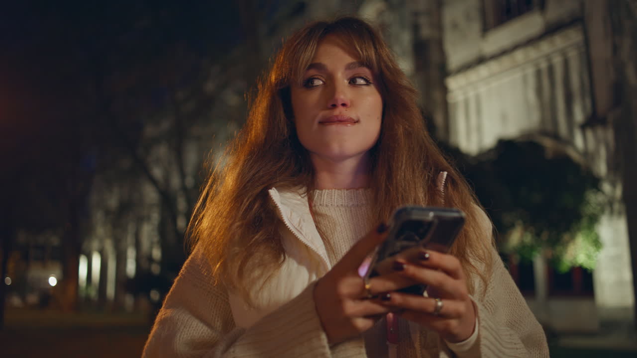 Donna riflessiva che usa il cellulare sotto i lampioni luminosi di strada di notte