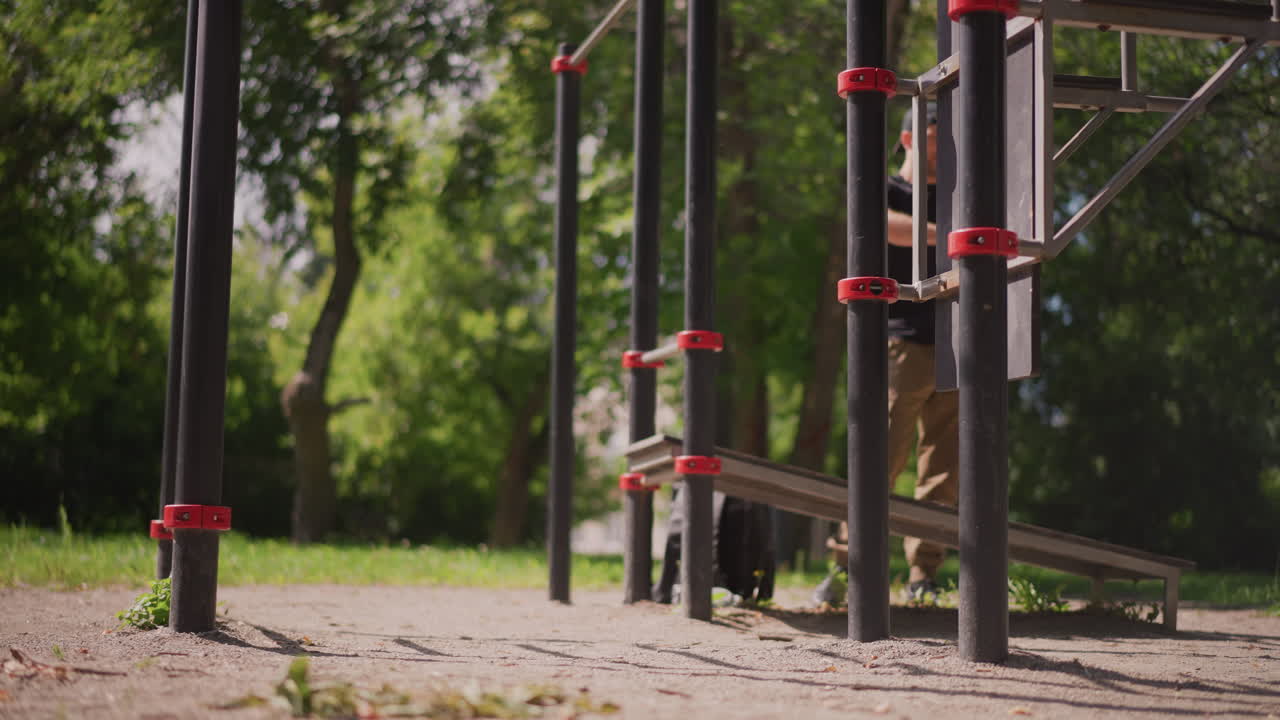 Man Rests Outdoors, Individual Relaxes While Walking Near Calisthenics Area In Park, Person Leisurely Walks Past Fitness Station In Park While Cooling Down After Vigorous Outdoor Exercise