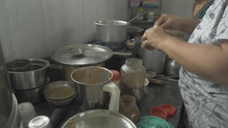 ángulo lateral de una mujer de mediana y avanzada edad que prepara curry tradicional de pollo y bhakri en la cocina india usando estufa de gas para cocinar