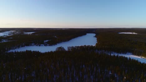 aerial drone view over snowy trees, towards a frozen lake, near hossa national park, on a sunny spring evening, in hossa, pohjois-pohjanmaa, finland