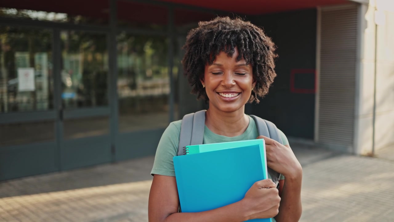Smilende afroamerikansk student holder mapper utenfor universitetet