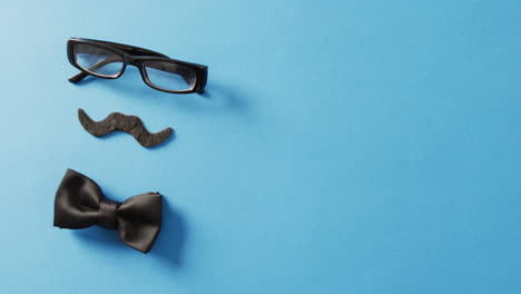 video de bigote falso, gafas negras y pajarita negra sobre fondo azul con espacio para copiar.