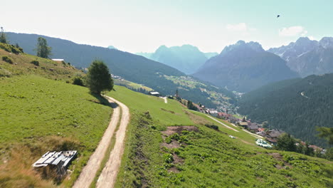 Video-De-Drones-Volando-Bajo-Sobre-El-Camino-De-La-Montaña-Y-Elevándose-Verticalmente-Hacia-La-Cordillera-De-Los-Dolomitas-En-Verano-Volando-Sobre-La-Histórica-Ciudad-De-Ladera-Rodeada-De-Bosques-Y-Tierras-De-Cultivo