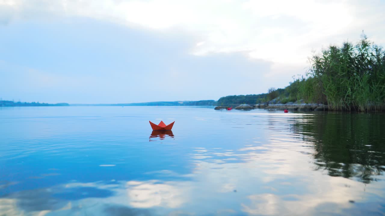 A paper boat floating away into the distance. Boat on the water. Beautiful sunset. Origami. River. Lake.