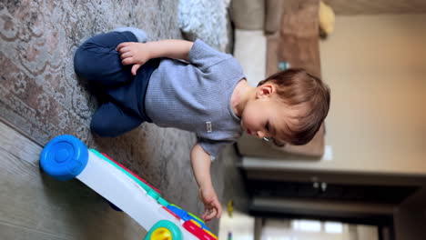 healthy caucasian baby boy playing in the room. adorable kid sits on the floor touching the toy with his finger. vertical screen.