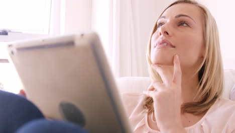 Blonde-woman-sitting-on-a-sofa-using-her-tablet