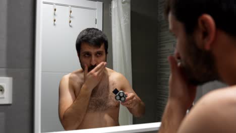 man turns electric shaver on to start shaving beard in bathroom mirror