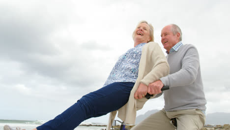 vista lateral de una pareja de ancianos caucásicos sentados en una bicicleta en la playa 4k