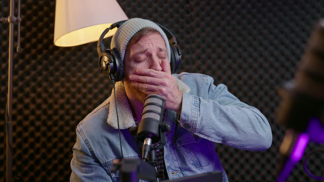 Bored and tired podcast or radio host looking at camera during live stream or interview trying to stay focused and awake. Getting sleepy and uninterested in sound studio listening to guest talking