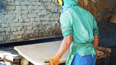 worker at stone cnc machine cutting the slab at stone factory. male worker in special clothers with mask and headphones putting slab into the machine.