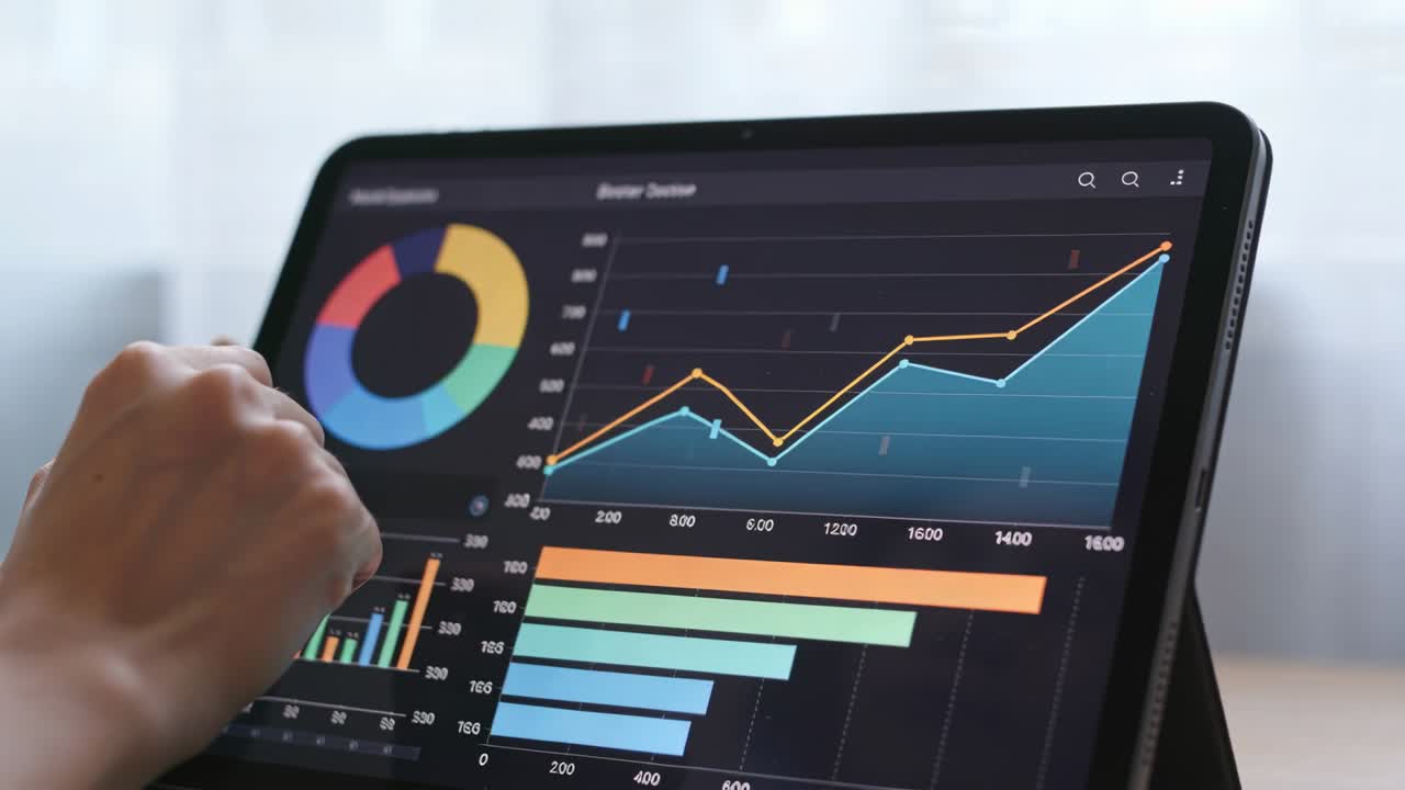 Pekende hånd fra venstre sjekker stigende trend på nettbrett ved skrivebord, holder folio-etui.