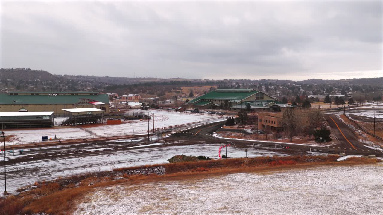 Thị trấn Castle Rock Colorado nhìn từ flycam, chuồng ngựa tại Hội chợ Douglas County, các tòa nhà phủ tuyết, buổi sáng mùa đông tuyết rơi, ngày nhiều mây, khu dân cư trung tâm thành phố, chuyển động lia máy sang trái