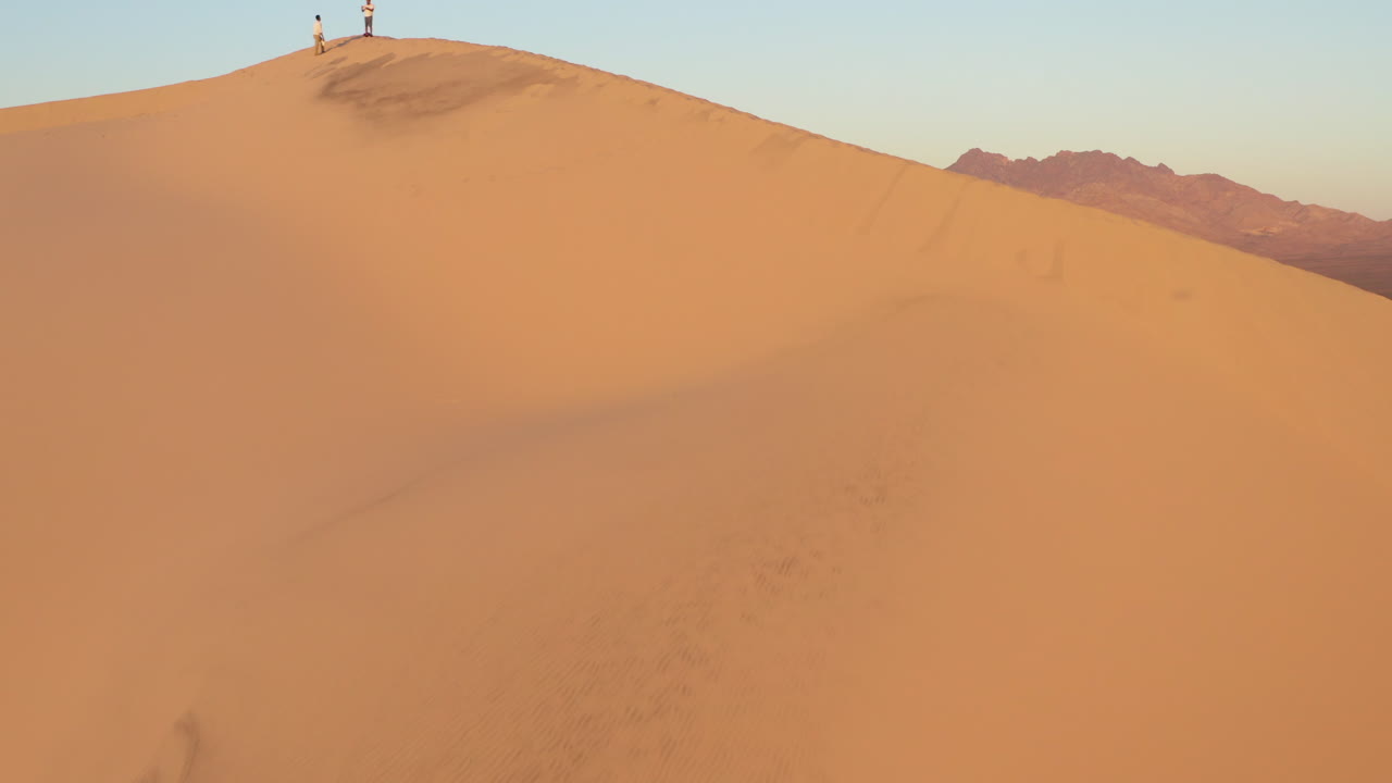 antena ascendente de una duna de arena en el desierto con 2 personas de pie en la cima de la montaña