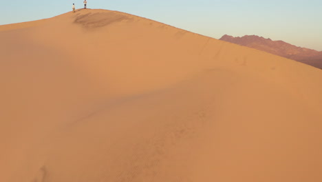 antena ascendente de una duna de arena en el desierto con 2 personas de pie en la cima de la montaña