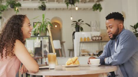 Happy-diverse-couple-spending-time-together-at-cafe,-drinking-coffee-and-talking